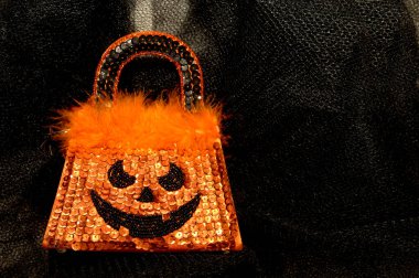 Cadılar Bayramı tasarımı çanta siyah ağ kumaş üzerinde yatar. Turuncu pullar yüzeyi süsler ve korkunç, başroldeki yüzü oluşturur. Turuncu boa tüyleri kenarı süslüyor.