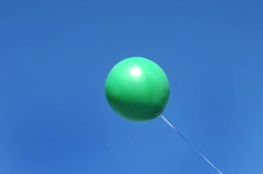 Yeşil balon açık mavi gökyüzünde süzülür.