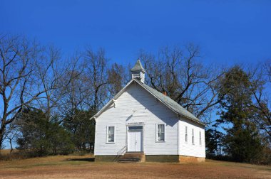 Bare trees cluster around Beulah Union Church as it sits in rural Northern Arkansas.  Church is wooden and painted white. clipart