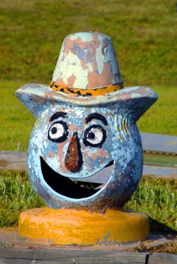 Gülen bir palyaçoyu çatırdatmış ve boyası soyulmuş. Şapkasında sarı bir kurdele var. Kırmızı burnu ve sarı yakası var..