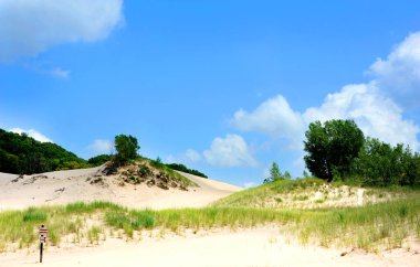 Tabelada ziyaretçilere Indiana Dunes Ulusal Parkı 'ndaki kum tepelerini korumak için yolda kalmaları talimatı veriliyor. Mavi gökyüzü tepelerin üzerinde süzülür.