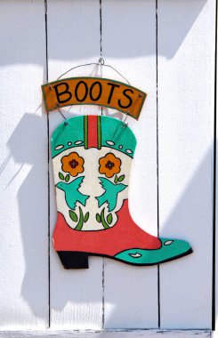 Colorful sign advertising boots for sale hands on a rustic white door in 