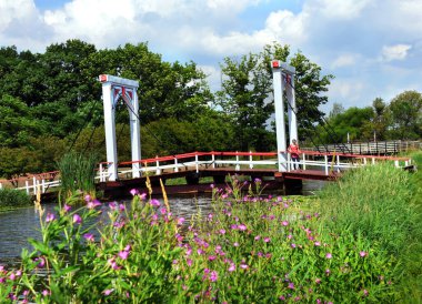 Attractive female tourist stands on the Dutch style bridge that crosses the Macatawa River in Dutch Island Gardens, Holland, Michigan.  Bridge is white with red trim. clipart