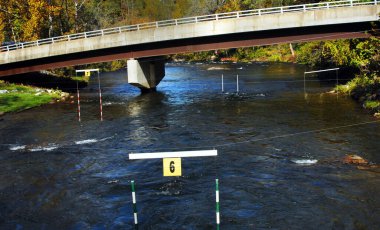 North Carolina river serves as practice course for Kayakers.  Obstacle course has hanging poles designating borders for manuevering.  Bridge crosses river behind course. clipart