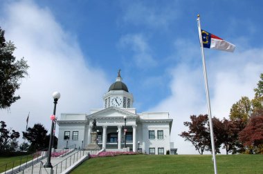 Elegant Jackson County Courthouse sits on a hill overlooking the town of Sylva, North Carolina.  North Carolina flag flies against a vivid blue sky. clipart