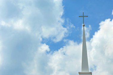 Çan kulesinde haç, beyaz bulutlar ve mavi gökyüzü tarafından çerçevelenir..
