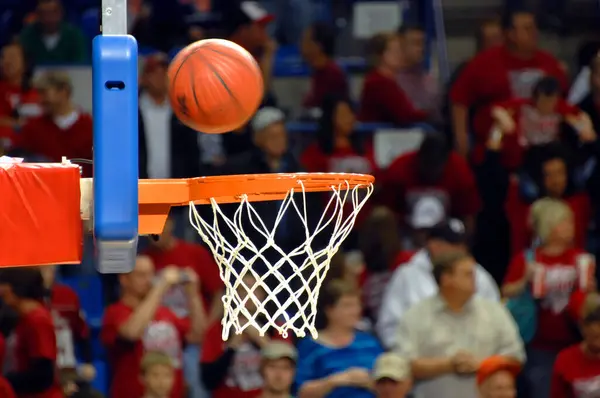 Dönen basketbol kaleye zıplamak için arka tahtayı kullanıyor. Kalabalık spor salonu lise basketbol maçını izliyor..