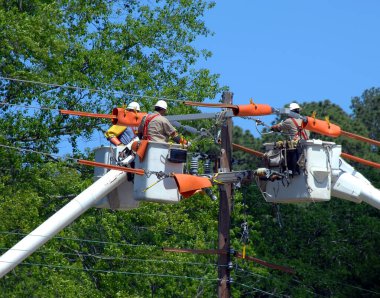 Üç kova kamyonu halat işçilerini elektrik direğinin tepesine çıkarıyor. Üç tamirci bilgi ve güç kesintisini birleştirir..  