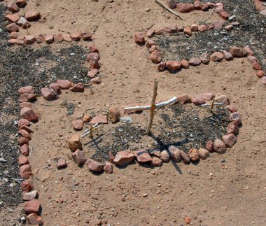 Tiny croses mark a tiny grave.  Sticks form croses and red stones surround grave. clipart