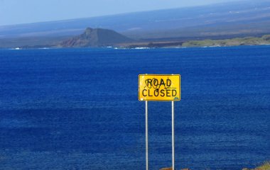 Bright yellow sign warns tourist that a road leading down to a beach, on the South Point of the Big Island of Hawaii, is closed. clipart