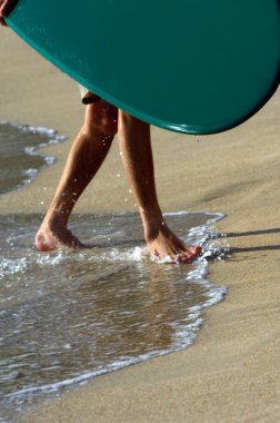 Sörfçü dalgalardan çıkar ve Oahu Adası 'ndaki Waikiki Sahili' nin kumlarına çıkar. Sörf tahtası yeşil ve ayakları su damlatıyor..