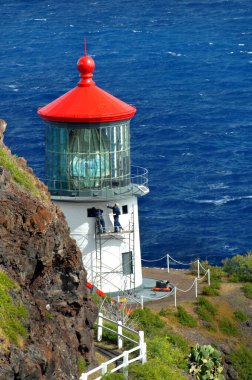 Two workmen paint the exterior of the Makapuu Point Lighthouse on the Island of Oahu, Hawaii.  Azure water frame cliff and light. clipart