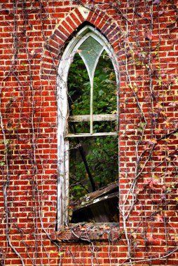 Arched window on abandoned church has one glass pane unbroken.  Debris shows through window from inside collapsing church. clipart