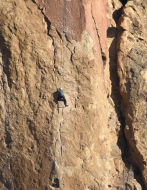 Dağcı, Smith Rock 'ın kayalık yüzeyine tutunuyor, Oregon' daki Smith Rock State Park 'ta. İp ve ekipman kullanarak tırmanıyor..