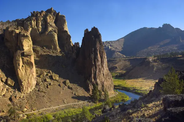 Güzel mavi gökyüzü Oregon 'daki Smith Rock State Parkı' nın üzerinde asılı. Eğri Nehir gökyüzünü yansıtır. Dağın eteklerinde rüzgarlar esiyor..