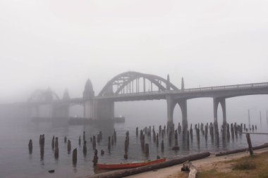Sabah sisi Oregon, Newport 'taki Yaquina Körfezi Köprüsü' nü kaplıyor. Kırmızı kayık karaya vurmuş çürüyen tahta kazıkların yanında..