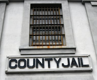 Beton bina eyalet hapishanesine ev sahipliği yapıyor. Paslı demir parmaklıklar pencereyi kapatır.