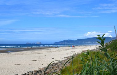 Cape Gözcü Parkı Sahili 'nde kum, su ve manzaranın tadını çıkaran ziyaretçiler var. Açıklar, Üç Kayalık Ulusal Vahşi Yaşam Sığınağı. Gökyüzü güneşli ve mavi.