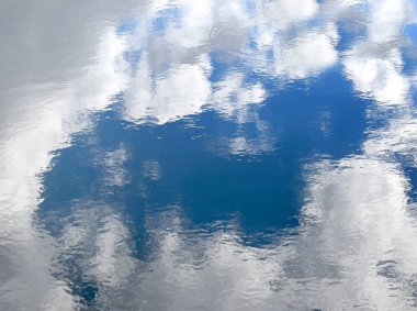 Küçük dalgalar Oregon 'daki bir göletin yüzeyini süslüyor. Beyaz bulutlar ve mavi gökyüzü yüzeye yansıyor.