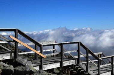 New Hampshire 'daki Washington Dağı' nın zirvesindeki ahşap basamaklar bulutlarla ve mavi gökyüzüyle çevrilidir..