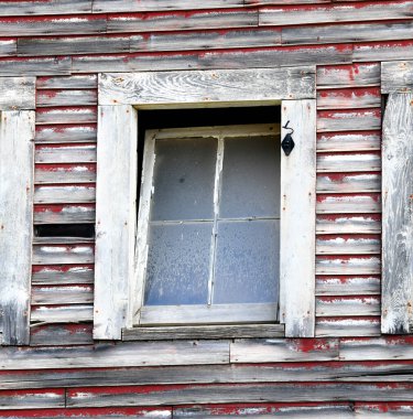 Yaşlı, yaşlı, kırmızı ahşap ambarın içinde eğim penceresi var. Ahır yıpranmış ve solmuş. Biraz da orijinal kırmızı boya kalmış..