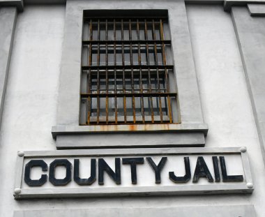 Beton bina eyalet hapishanesine ev sahipliği yapıyor. Paslı demir parmaklıklar pencereyi kapatır.