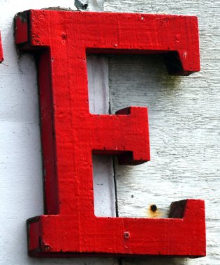 Büyük, kırmızı ahşap bir E beyaz boyalı bir sedye üzerine monte edilir. E soyuluyor ve arka tahtası soyuluyor..
