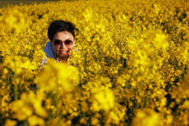 Güneşin batışında kolza tohumu tarlasında gülümseyen orta yaşlı kadın.