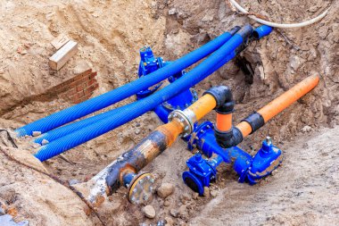 Blue and orange water pipes and cable conduits in a pit. Repair work is underway on city utilities clipart