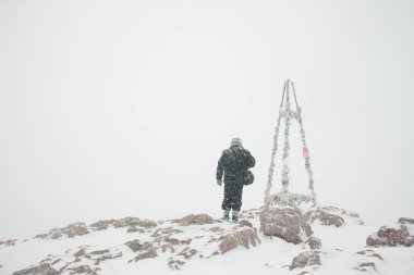 Adam yoğun karda dağın zirvesine ulaştı. Dağın en yüksek noktasında kurdelelerle asılı bir dönüm noktası