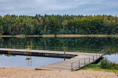 A deserted beach with a pier on a forest lake. High quality photo clipart