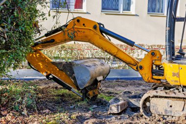 Sarı bir parça, bir binanın önünde kovayla takip edilmiş mini kazıcı. Yüksek kalite fotoğraf