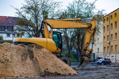 Sarı bir kazıcı ev ve arabaların arka planında büyük bir kil yığınının arkasında duruyor. Yüksek kalite fotoğraf