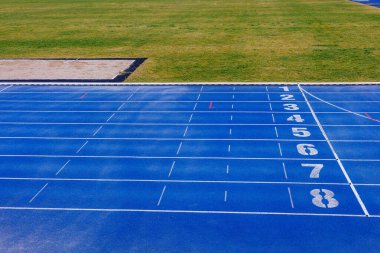 Beyaz rakamlı mavi raylar. Yeşil yapay çimenli futbol sahası. Uzun atlama için kum çukuru. Yüksek kalite fotoğraf