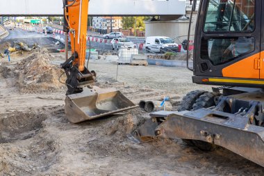 Elinde kova olan bir kazıcı bir yol kavşağının arka planında duruyor. Yüksek kalite fotoğraf