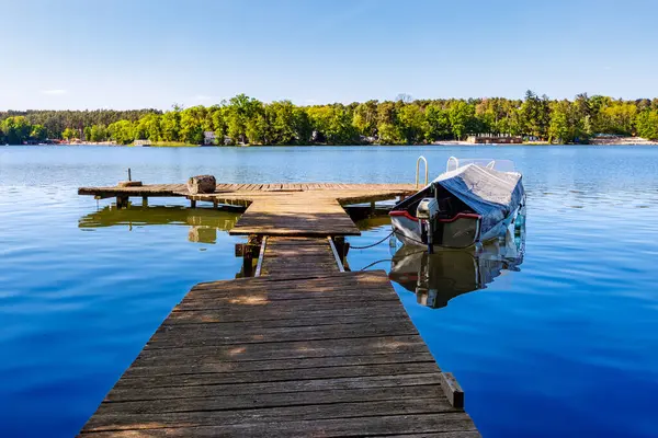 Küçük bir gölün kıyısına bağlı branda kaplı bir motorlu tekne ile sağlam ahşap bir köprü. Yüksek kalite fotoğraf