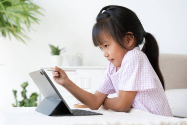 Education. Asian little girl learning and drawing with the online teacher on tablet digital, Application on mobile at home morning, Side view
