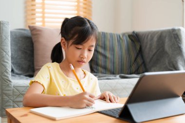 Asyalı küçük kız ödev yapıyor, öğreniyor, dijital tablet kullanıyor. Evde eğitim, evde online öğrenim kavramı