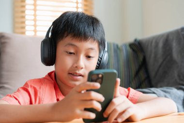 Excited Asian boy playing online game on smart phone with headphones. Asia man using mobile phone happy smile at home  in morning 