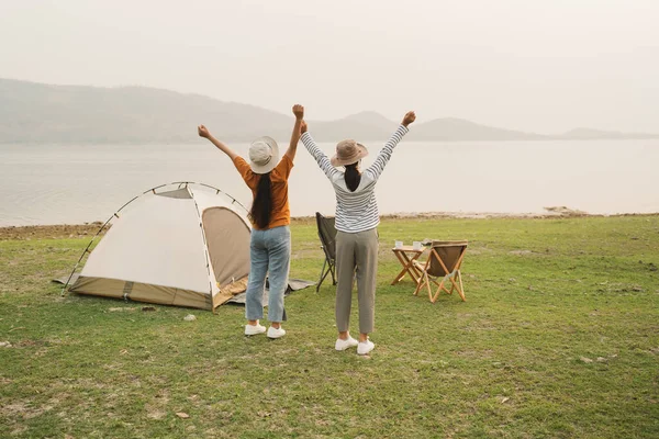 后视镜亚洲两个少女举手看着河 亚洲少女在夕阳西下的草地上和高山上快乐地笑着 生活方式 度假和自由的概念露营 图库图片