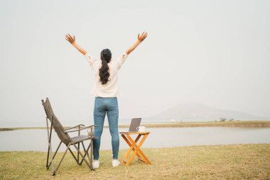 Arkadan bak. Asyalı kadın nehre bakarken elini kaldırdı. Mutlu Asyalı kadınlar kamp alanında çalıştıktan sonra dinleniyor. Yaşam tarzı tatili ve özgürlük kampı kavramını