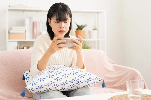 亚洲女人玩在线游戏 通过智能手机的互联网进行现场直播 亚洲妇女早上坐在沙发上用手机 图库照片