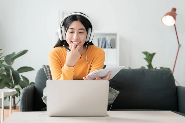 在家学习 亚洲女孩在网上通过网络学习视频会议 电脑辅导 亚洲妇女在家里早上使用带耳机的笔记本电脑 图库图片