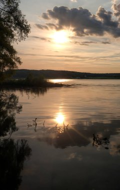 Güneşin son ışınlarının suda altın-pembe bir parıltı oluşturduğu bir nehrin üzerinde sihirli bir günbatımı. Sakin bir nehir yüzeyi. Doğa, seyahat, meditasyon veya ilham konseptleri için.