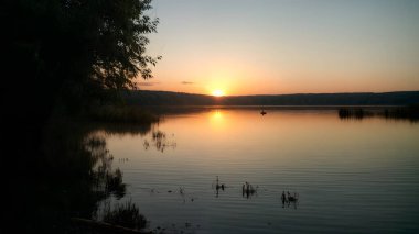 Güneşin son ışınlarının suda altın-pembe bir parıltı oluşturduğu bir nehrin üzerinde sihirli bir günbatımı. Sakin bir nehir yüzeyi. Doğa, seyahat, meditasyon veya ilham konseptleri için.