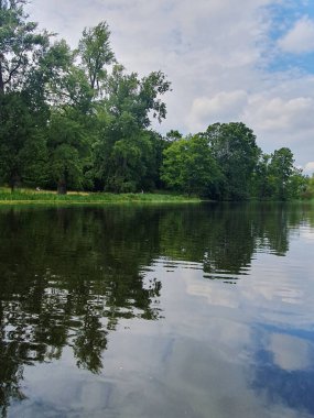 Yoğun yeşil bir ormanla çevrili sessiz bir nehir ya da göl. Aynaya benzeyen su, ağaçları ve gökyüzünü yansıtır. Doğayla bir barış ve birlik ortamı yaratır. Bulutlu açık yaz gökyüzü