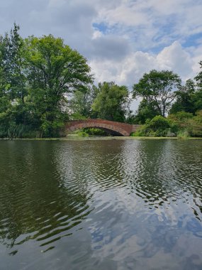 Yoğun yeşil bir ormanla çevrili sessiz bir nehir ya da göl. Aynaya benzeyen su, ağaçları ve gökyüzünü yansıtır. Doğayla bir barış ve birlik ortamı yaratır. Bulutlu açık yaz gökyüzü