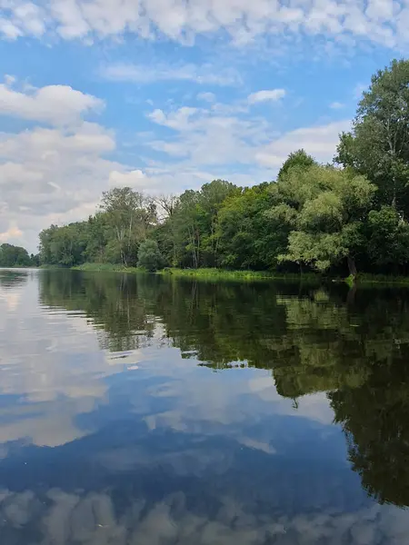 Yoğun yeşil bir ormanla çevrili sessiz bir nehir ya da göl. Aynaya benzeyen su, ağaçları ve gökyüzünü yansıtır. Doğayla bir barış ve birlik ortamı yaratır. Bulutlu açık yaz gökyüzü