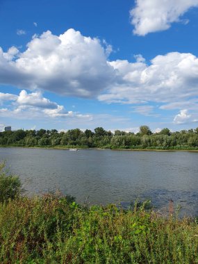 Yoğun yeşil bir ormanla çevrili sessiz bir nehir ya da göl. Aynaya benzeyen su, ağaçları ve gökyüzünü yansıtır. Doğayla bir barış ve birlik ortamı yaratır. Bulutlu açık yaz gökyüzü