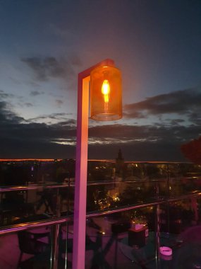 Açık bir yaz gününde çekilen panoramik şehir manzarası. Gökyüzü, binlerce ışığın sıcacık parıltısıyla mimariyi aydınlatıyor. Metropolün ve gece hayatının enerjisini taşır.